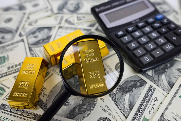 gold bars lie with a calculator and a magnifying glass next to a large amount of dollars. Financial saving concept. gold and dollars.