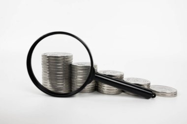 Büyüteç beyaz arka planda para yığını kavramını büyütüyor. Mali konsept