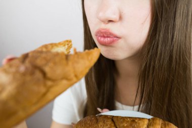 young beautiful girl eating a croissant, close-up, crop photo.