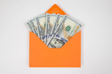 Beyaz arka planda izole edilmiş dolarlarla dolu turuncu bir zarf. Zarfın içinde dolar var..