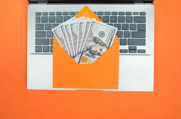 laptop and orange envelope with dollars on an orange background.