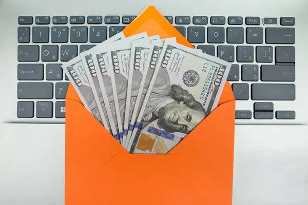 laptop and orange envelope with dollars on an orange background.