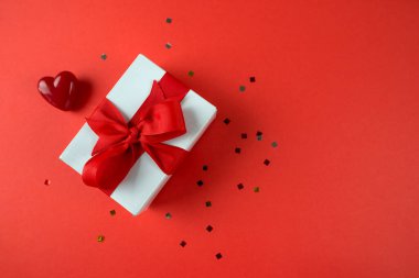 Hediye kutusunun en üstteki fotoğrafı ve kırmızı arka planda bir kalp. Mesaj için yer. Sevgililer Günü konsepti.