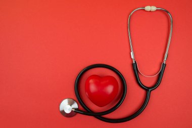 Tıbbi steteskop ve kırmızı kalp fotokopi alanı ile kırmızı zemin üzerinde.