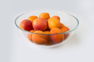 beyaz zemin üzerinde bir cam kasede olgun kayısı