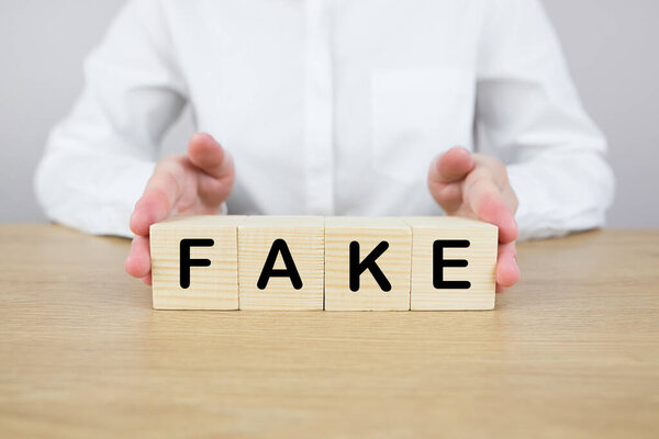 Женщина сидит за столом и держит кубики со словом подделка. Фото с урожая.