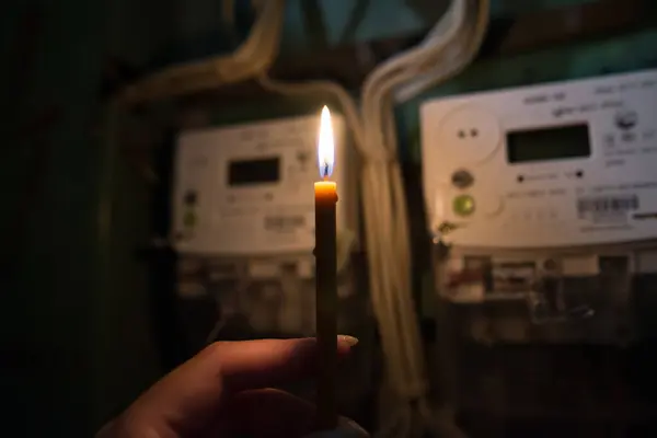 Karanlıkta elinde mum olan bir el evdeki elektrik sayacına bakar. Elektrik kesintisi, karartma konsepti