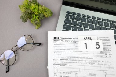 Gri arka planda dizüstü bilgisayarı ve diğer ofis malzemeleriyle dolu 1040 vergi formu. Üst görünüm.