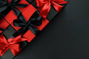 Kırmızı saten kurdeleli siyah hediye kutularının üst görünümü kopyalanmış siyah arkaplan üzerinde