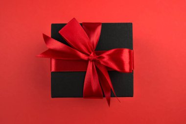 İzole edilmiş kırmızı zemin üzerinde kırmızı yay ve boş boşluk olan siyah hediye kutusunun üst görünümü
