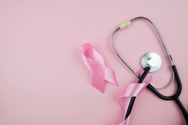 Top view photo of pink ribbon symbol of breast cancer awareness and stethoscope on isolated pastel pink background with copyspace