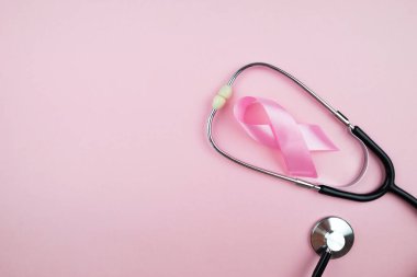 Top view photo of pink ribbon symbol of breast cancer awareness and stethoscope on isolated pastel pink background with copyspace