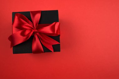 İzole edilmiş kırmızı zemin üzerinde kırmızı yay ve boş boşluk olan siyah hediye kutusunun üst görünümü