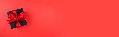 Kara Cuma indirim konsepti. Kırmızı arka planda kırmızı saten kurdeleli siyah hediye kutusu. Uzayı kopyala Pankart.