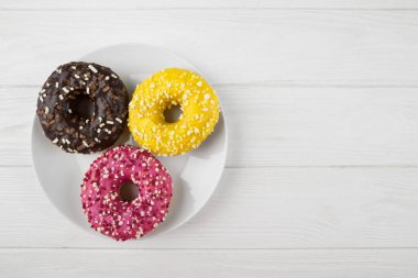 Beyaz ahşap bir masada beyaz bir tabakta farklı jöleli üç çörek. Üst görünüm.