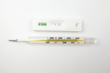 Pozitif Covid-19 antijen testi ve termometre. Beyaz zemin üzerinde hızlı koronavirüs antijen testi ve elektronik termometre.