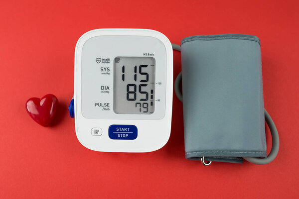 red heart and electronic tonometer on a red background.