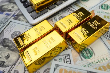Altın külçeleri, izole edilmiş büyük miktarda doların yanında bir hesap makinesiyle yatar. Finansal tasarruf kavramı. Altın ve Dolar.