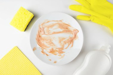 Beyaz arka planda izole edilmiş bulaşık yıkamak için kırmızı soslu beyaz kirli tabak ve sünger. Temizlik konsepti. Yemek yedikten sonra bulaşık ve yemek lekelerini temizlemek için temizlik süngeri.