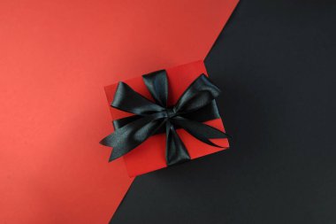 Siyah kırmızı arka planda siyah kurdeleli hediye kutusu. Kara Cuma konsepti, satış, promosyonlar, indirimler, Noel tatilleri