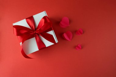 Kırmızı arka planda kırmızı fiyonklu beyaz hediye kutusu.