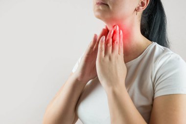 Farenjit, bademcik iltihabı. Beyaz tişörtlü bir kadının boğaz ağrısı çekerken çekilmiş fotoğrafı. Yutkunurken, boyna dokunurken, bej arka planda izole edilmiş ve fotokopi alanı olan.