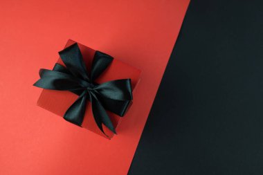 Siyah kırmızı arka planda siyah kurdeleli hediye kutusu. Kara Cuma konsepti, satış, promosyonlar, indirimler, Noel tatilleri