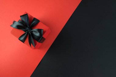Siyah kırmızı arka planda siyah kurdeleli hediye kutusu. Kara Cuma konsepti, satış, promosyonlar, indirimler, Noel tatilleri