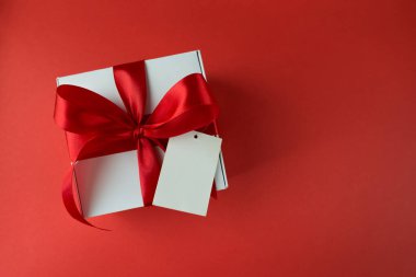 Kırmızı arka planda kırmızı fiyonklu beyaz hediye kutusu.