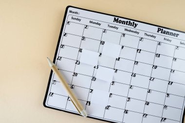 Takvim. Yapışkan notlu takvim sayfası, bej arkaplanlı kalem, üst görünüm. Mesaj için yer var. Planlayıcı.