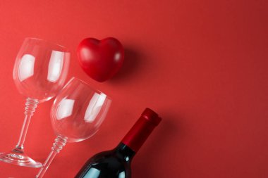 Sevgililer Günü için kırmızı arka planda kadehler ve bir şişe kırmızı şarap.
