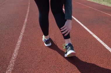 Atletik bayan koşucunun ayak bileği burkulduğu için bacağına dokunduğu fotoğraf, arka görüş. Koşu sporu, eğitim sakatlığı