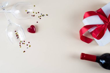 Sevgililer Günü konsepti, beyaz fotoğraf çerçevesi, iki kadeh şarap, hediye kutusu, bir şişe şarap, bej arka planda kalp. Boşluğu kopyala, metin için yer.