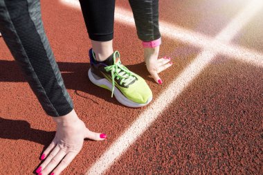 Stadyumda çömelmiş genç bir bayanın bacakları başlangıç pozisyonunda, yaklaşın. Üst görünüm
