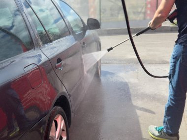 Araba yıkama işlemine yakın çekim. Adam arabasına su akıntısı ile hortum çekiyor, araba yıkamada araba yıkıyor. Araba yıkama konsepti. İnsanlar ve ulaşım