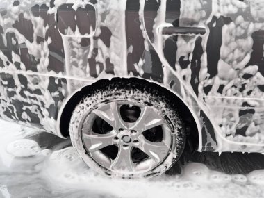 Araba yıkama yerindeki köpüklü araba tekerine yakın çekim. Araba yıkama konsepti.