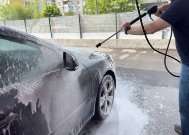 Erkek sürücünün otomobil yıkama servisinde yüksek basınçlı su jeti ile arabasını yıkaması..