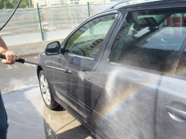 Erkek sürücünün otomobil yıkama servisinde yüksek basınçlı su jeti ile arabasını yıkaması..