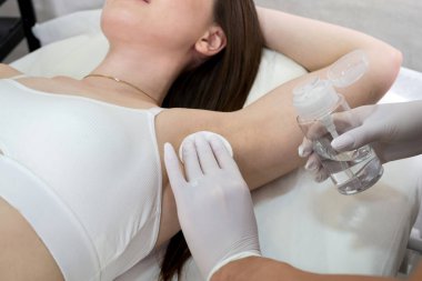 Kuafördeki kadın, kozmetik uzmanı koltuk altlarını pamukla siliyor. Kozmetoloji prosedürü için koltuk altları hazırlanıyor