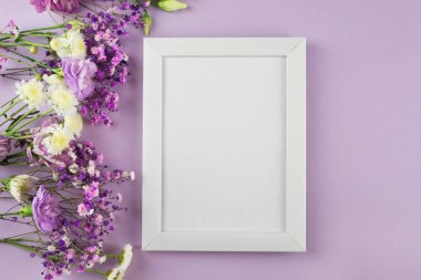 Mor pastel arka planda çiçeklerle süslenmiş fotoğraf çerçevesi. Metin için boş alan. Kopyalama alanı olan bir model. Düz yatıyordu. Beyaz fotoğraf çerçevesi, afiş. Kartpostal, Anneler Günü, 8 Mart.