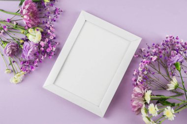 Mor pastel arka planda çiçeklerle süslenmiş fotoğraf çerçevesi. Metin için boş alan. Kopyalama alanı olan bir model. Düz yatıyordu. Beyaz fotoğraf çerçevesi, afiş. Kartpostal, Anneler Günü, 8 Mart.