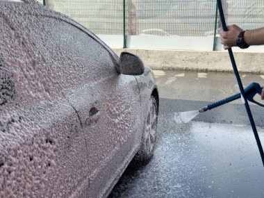 Erkek sürücünün otomobil yıkama servisinde yüksek basınçlı su jeti ile arabasını yıkaması..