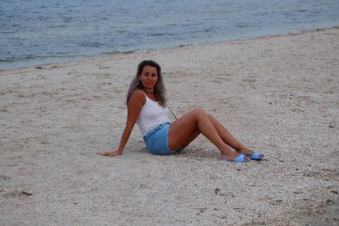 Tatil kumsalındaki kadın fotoğraf çekimi yapıyor farklı pozlar ve mekanlarda gülümsüyor sarı saçlı hasır şapka farklı çekim seçenekleri sunuyor güneşlenmeler deniz ve kumda yürüyor.