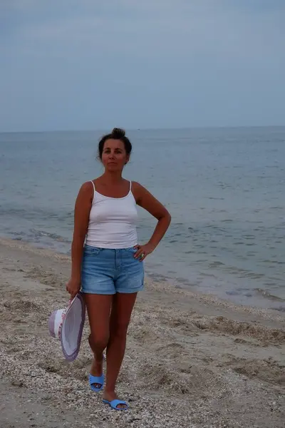 Tatil kumsalındaki kadın fotoğraf çekimi yapıyor farklı pozlar ve mekanlarda gülümsüyor sarı saçlı hasır şapka farklı çekim seçenekleri sunuyor güneşlenmeler deniz ve kumda yürüyor.