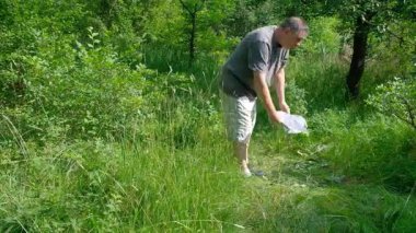 Ormanda orta yaşlı bir adam kareli şortlu ve beyaz şapkalı turistle yürürken yavaşça hava soluyor. Yüksek kalite 4K görüntü. Spor yapan orta yaşlı bir adam spor yapıyor. Bacak kaldırıyor, sağlık sporlarını eğiyor. Yapabilirsin.