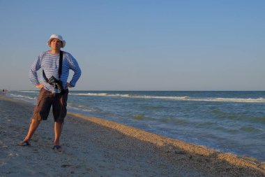 Orta yaşlı bir adam yazın deniz kıyısında yürüyor, kamera ile ve uzaktaki doğanın güzelliğinin fotoğraflarını çekiyor insanların deniz bulutları 1 'i görebiliyorsunuz.
