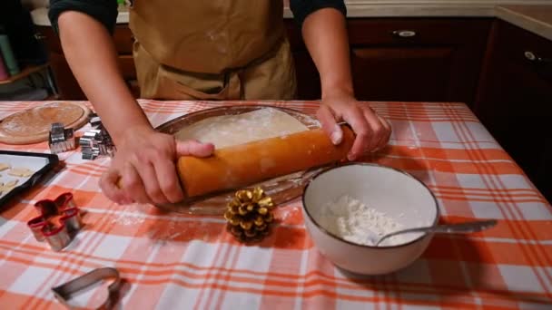 最上階だ 女性主婦の手 ベージュシェフのエプロンを着たシェフの菓子職人は 圧延ピンを使用して 木製の板の上にジンジャーブレッド生地を展開します テーブルの上に寝そべってる — ストック動画