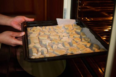 Ev hanımı bir fırıncının ellerine seçici bir odak noktası, sıcak fırına oyulmuş zencefilli ekmek hamuru kalıpları ile bir yemek tepsisi koymak, Noel yemeği için lezzetli ev yapımı kurabiyeler yapmak. Aile Gelenekleri