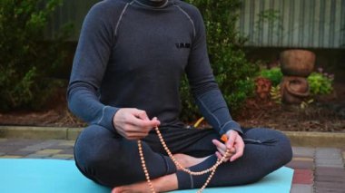 Sporcu, atletik bir adam, gri spor giyimli bir yogi, mavi bir spor minderinde poz veren, meditasyon yaparken kutsal tespih taşıyan, gün batımında yoga yapan