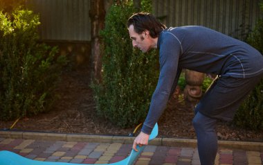 Yakışıklı beyaz adam, aktif erkek atlet, sporcu gün batımında dışarıda yoga yapmak ve egzersiz yapmak için spor minderi açıyorum. Aktif ve sağlıklı yaşam tarzı kavramı. Spor Sporu Sporu Çalışması